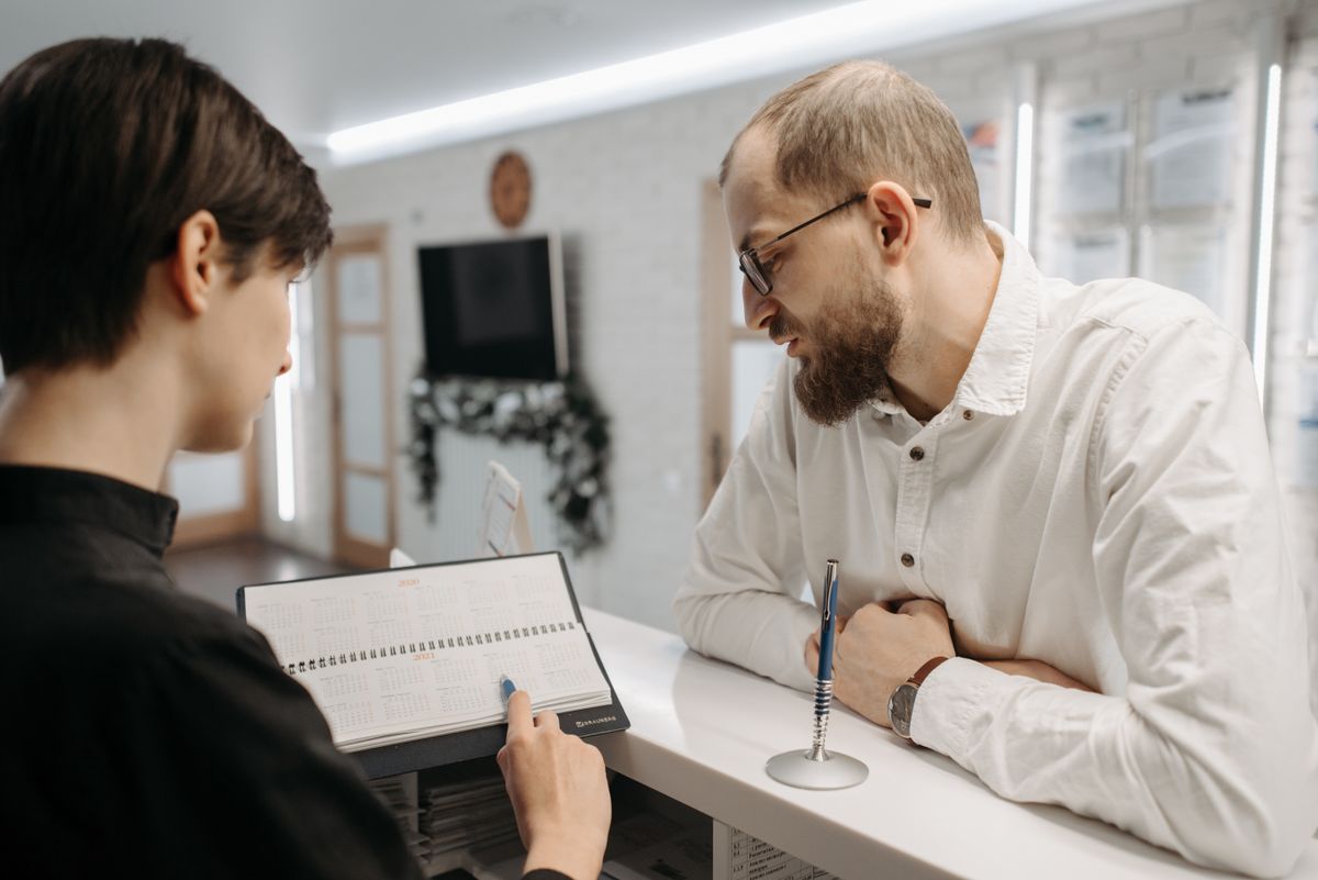 Eine Rezeptionistin bespricht mit einem Patienten am Empfang einen Termin im Kalender